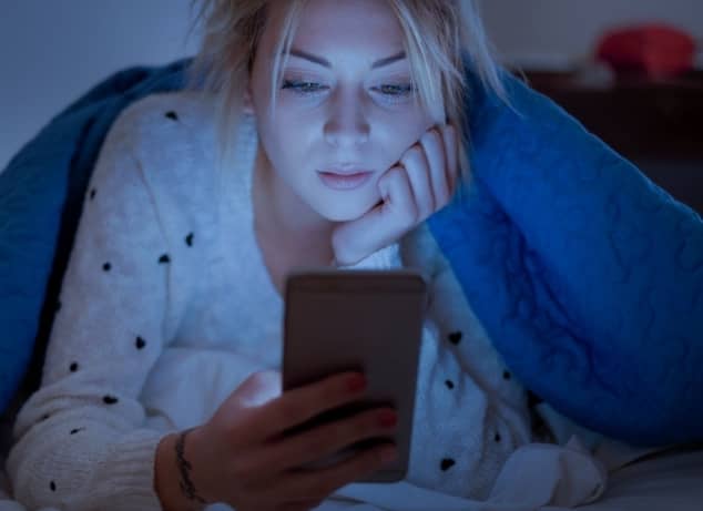 Chica en la cama con ropa de dormir y luces apagada escribiendo mensajes de texto en conversación íntima con el hombre que le gusta