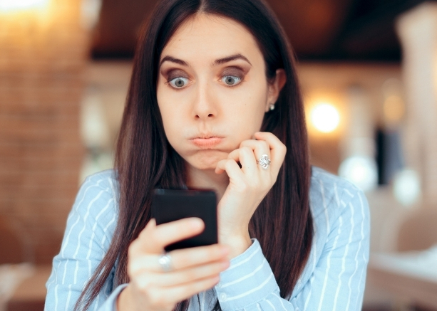 Chica mirando su celular con expresión de aturdida debido a que algún chico se pasa de la ralla con la cantidad de mensajes de texto que le escribe
